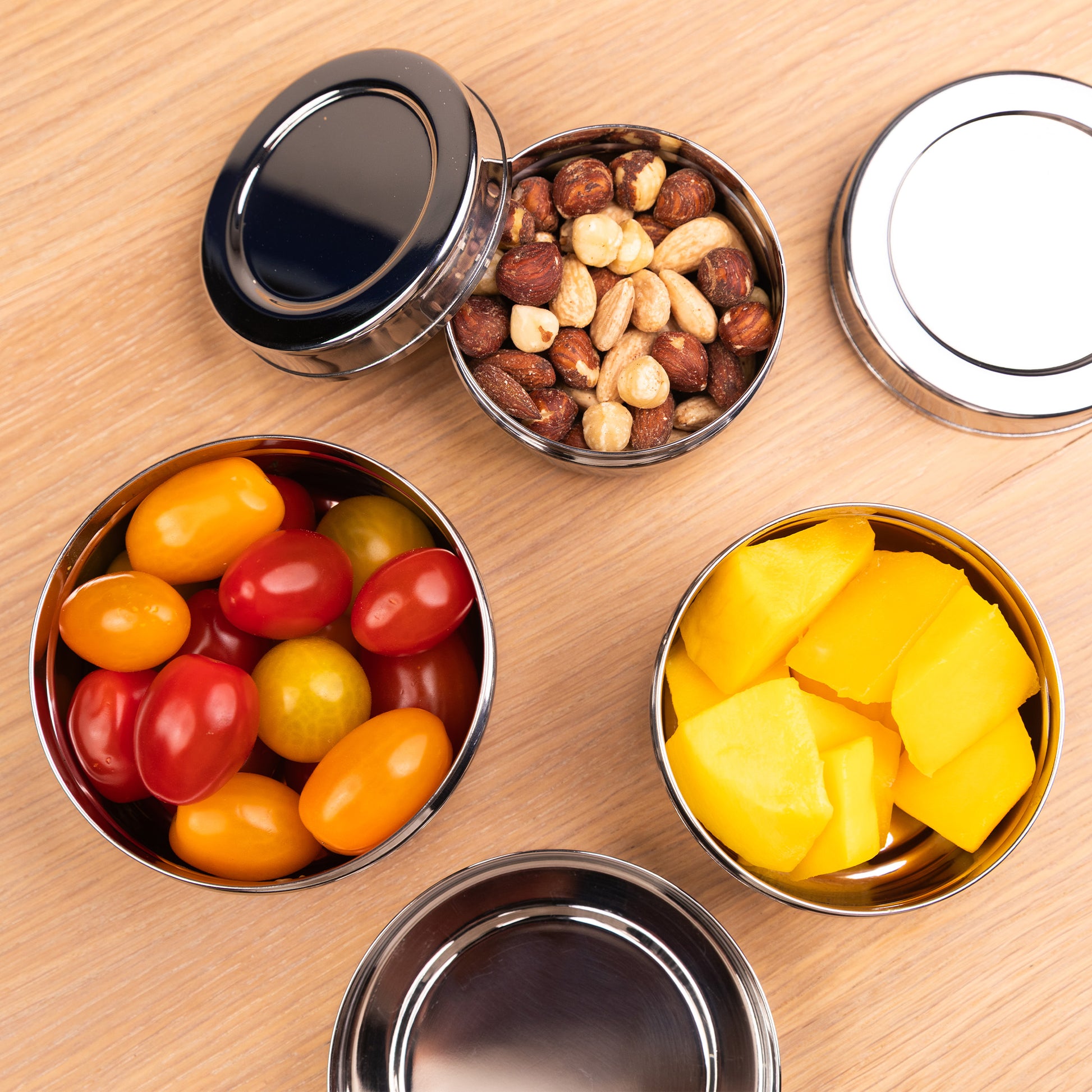 RVS snackboxen gevuld met noten, tomaten en mango