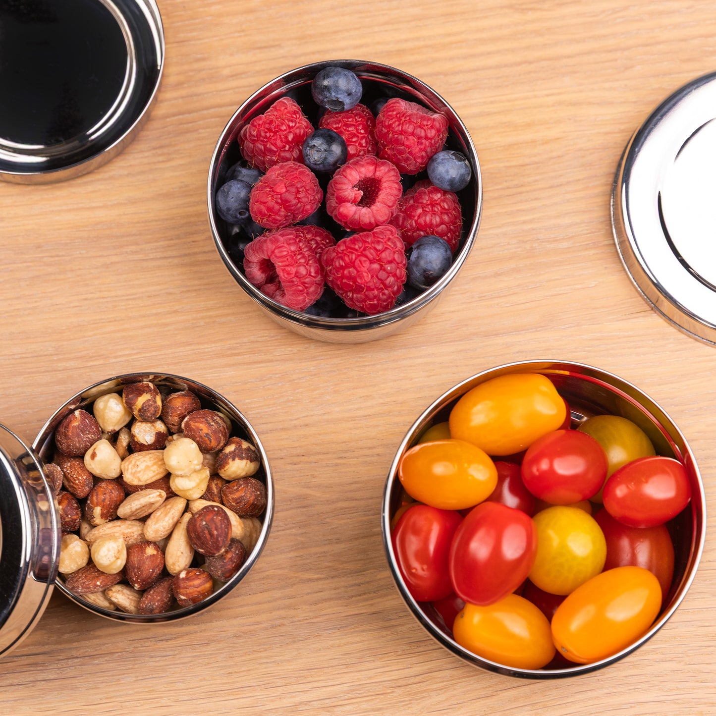 3 RVS snackboxen gevuld met fruit op een schooltafel